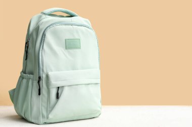 Yeşil okul sırt çantası sarı duvarın yanındaki beyaz grunge masasında.