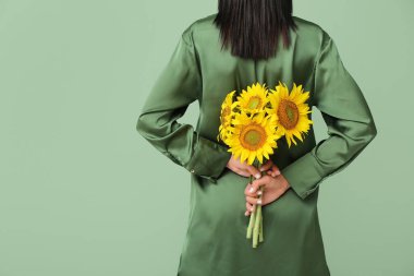Young woman with beautiful sunflowers on green background, back view