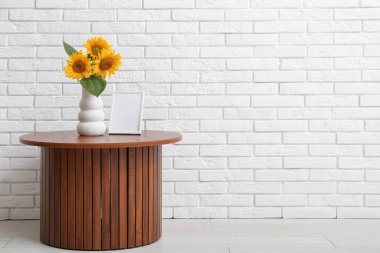 Güzel ayçiçekleri olan vazo ve boş çerçeve odanın duvarının yanındaki masada.