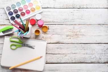 Boş defter, renkli kalemler ve beyaz ahşap zemin üzerine boyalar içeren kompozisyon
