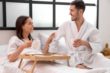 Yatağında kahve fincanları olan mutlu genç çift.