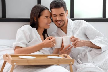 Yatağında kahve fincanları olan mutlu genç çift.