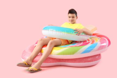 Şişirilebilir yüzüklü ve pembe arka planda şilteleri olan şirin, mutlu bir çocuk.