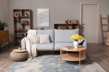 Interior of stylish living room with grey sofa, plaid, coffee table and flowers