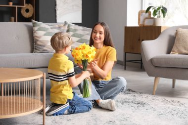 Son greeting his happy mother with bouquet of beautiful narcissus at home