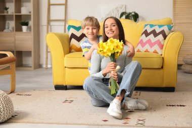 Happy woman and her little son with bouquet of beautiful narcissus at home