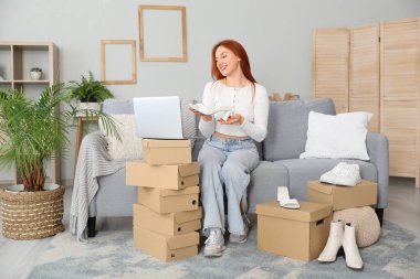 Evde yeni ayakkabılar denerken dizüstü bilgisayar kullanan genç bir kadın.