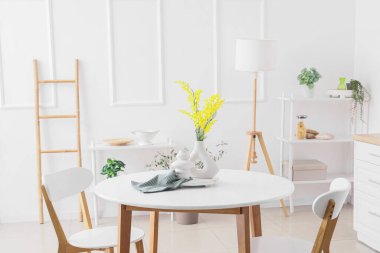 Hafif mutfaktaki yemek masasında mimoza çiçekleri olan vazo.