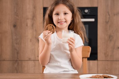 Mutfakta bir bardak süt ve kurabiyeyle küçük tatlı bir kız.