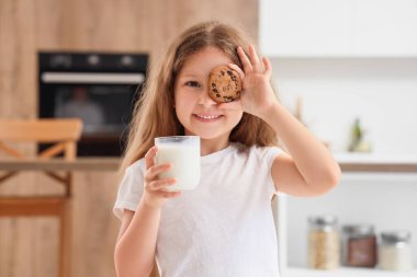 Mutfakta bir bardak süt ve kurabiyeyle küçük tatlı bir kız.