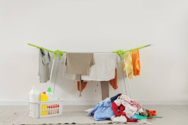 Kurutucu, kirli çamaşır yığını ve çamaşır deterjanı beyaz duvarın yanında.