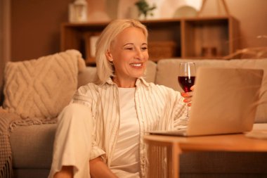 Şarap ve dizüstü bilgisayarı olan olgun bir kadın akşam evde randevusu var.