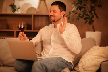 Şarap ve dizüstü bilgisayarı olan yakışıklı bir adamın akşamları evdeki kanepede randevusu var.