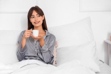 Genç ve güzel bir bayanın bir fincan kahveyle yatak odasında uzandığı bir sabah.