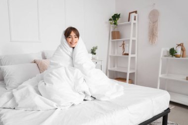 Yatak odasında, yumuşak battaniyeli güzel genç bir kadının oturduğu sabah.