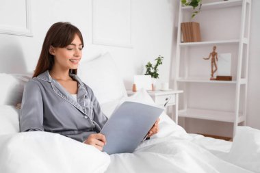 Güzel genç bir kadının yatak odasında dergi okuduğu bir sabah.