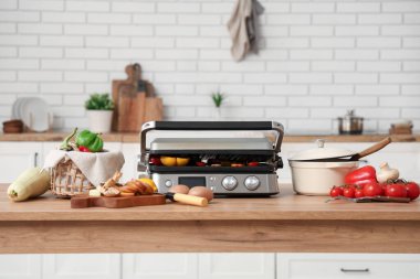 Kapalı modern elektrikli ızgara, lezzetli sebzeler, tencere ve sepet mutfakta.