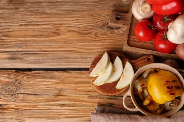 Izgara sebzeli tencere ve ahşap arka planda taze sebzeli tepsiler.