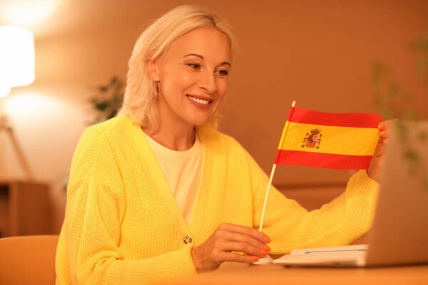 Mature woman with flag of Spain learning language online at home in evening