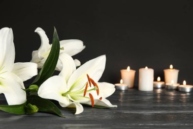 Güzel beyaz zambak çiçekleri ve koyu ahşap masada yanan mumlar.