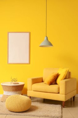 Oturma odasının içinde kolye lambası, sarı koltuk ve boş çerçeve