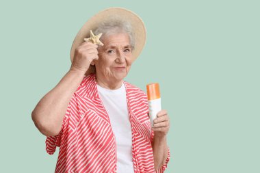Yeşil arka planda güneş kremi ve deniz yıldızı olan yaşlı bir kadın.