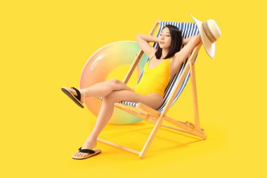 Güzel Asyalı kadın sarı arka planda iskemlede dinleniyor.