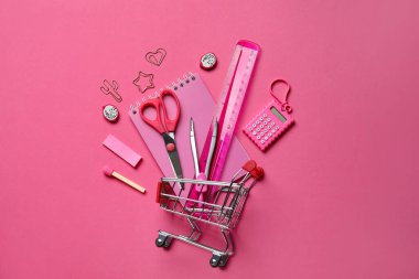 Alışveriş arabalı kompozisyon ve pembe arka planda farklı kırtasiye malzemesi