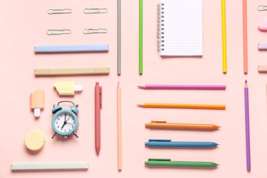 Pembe arka planda farklı kırtasiye malzemesi içeren defter.