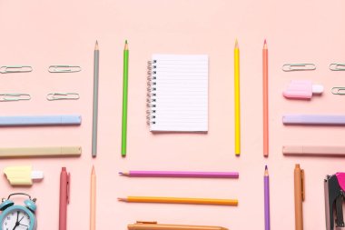 Pembe arka planda farklı kırtasiye malzemesi içeren defter.