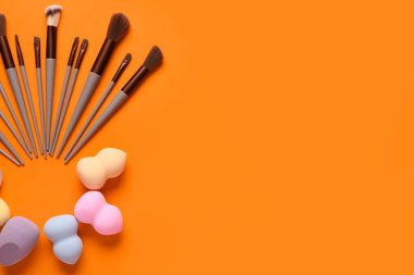 Turuncu arka planda makyaj süngerleri ve fırçalar
