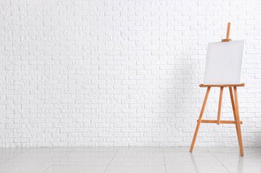 Beyaz tuğla duvarın yanında boş tuval olan ahşap sehpa