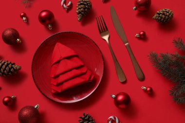 Kırmızı arka planda katlanmış peçete ve Noel süslemeleri olan şölen masası ayarları, yakın plan