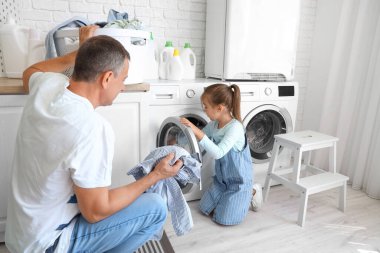 Küçük torunuyla evde çamaşır yıkayan olgun bir adam.