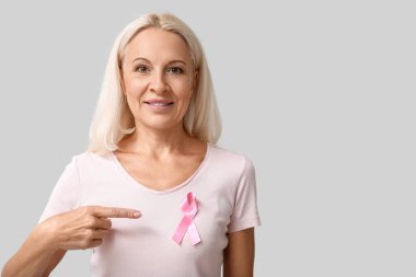 Gri arka planda pembe kurdeleli olgun bir kadın. Göğüs kanseri farkındalığı konsepti