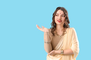 Sari giymiş güzel bir Hintli kadın mavi arka plandaki bir şeyi işaret ediyor.