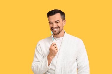 Sarı arka planda diş fırçası olan yakışıklı bir adam.