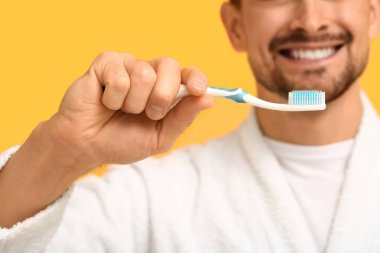 Sarı arka planda diş fırçası olan yakışıklı adam, yakın plan.
