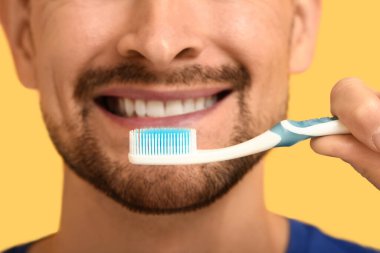 Sarı arka planda diş fırçası olan yakışıklı adam, yakın plan.