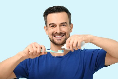 Mavi arka planda diş macunu sıkan yakışıklı adam.