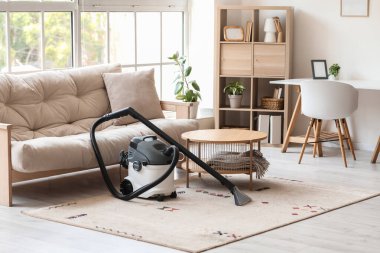 Aydınlık oturma odasındaki halının üzerinde modern elektrikli süpürge.