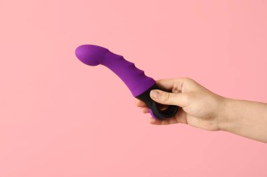 Pembe arka planda mor vibratörlü kadın el, yakın plan.