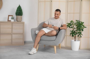 Nabız oksimetresi olan sportif genç adam evdeki koltukta oturuyor.