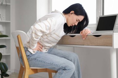 Dizüstü bilgisayarı olan genç bir kadın evinde şiddetli karın ağrısı çekiyor.