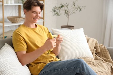 Evdeki kanepede muz soyan genç adam.