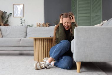 Evdeki kanepenin yanında panik atak geçiren genç bir kadın.