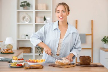 Güzel, genç ve mutlu bir kadın evde tereyağlı tost ekmeği kesiyor.
