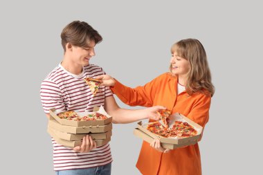 Gri arka planda lezzetli pizzalarla dolu karton kutular taşıyan güzel genç bir çift.