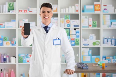 Eczanede cep telefonu olan bir erkek eczacı.