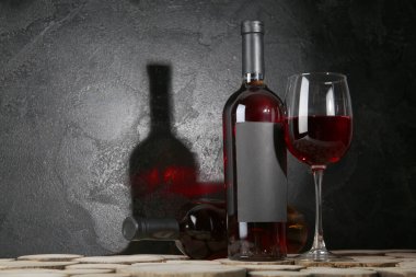 Siyah grunge arka planına karşı ahşap masada şişe ve bir bardak kırmızı şarap.